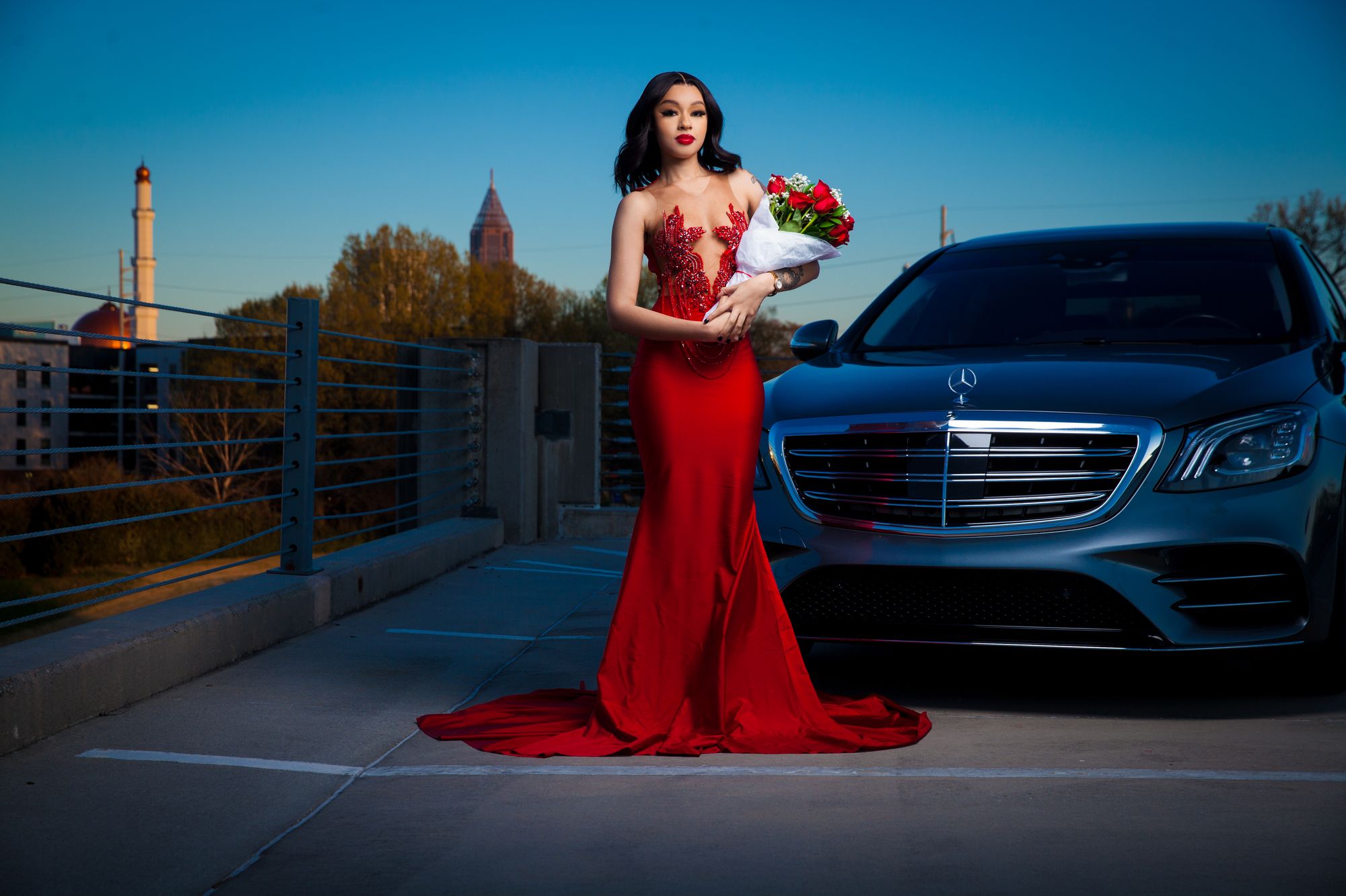 A woman in a red gown posed beside a classic car